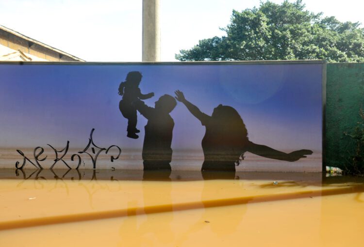 Imagem da silhueta de um casal com seu filho pequeno pintada em um muro que está sob a enchente do Rio Grande do Sul. Jornal UFRGS - Crédito Flavio Dutra